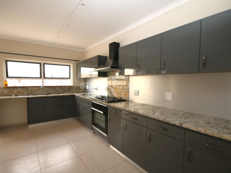 Modern kitchen featuring dark grey cabinetry, granite countertops, built-in oven, gas hob, and extractor fan with tiled flooring.