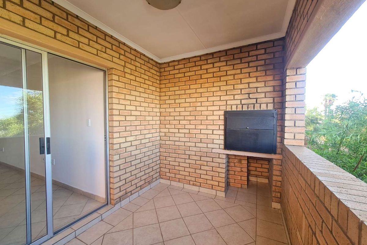 A covered balcony featuring face-brick walls, tiled flooring, and a built-in braai, providing a functional outdoor entertainment space.