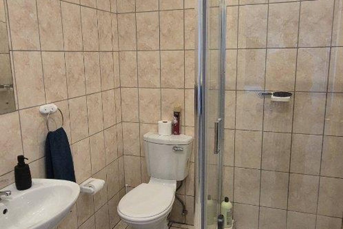 A functional bathroom featuring a glass-enclosed shower, pedestal basin, and toilet with neutral wall and floor tiling.