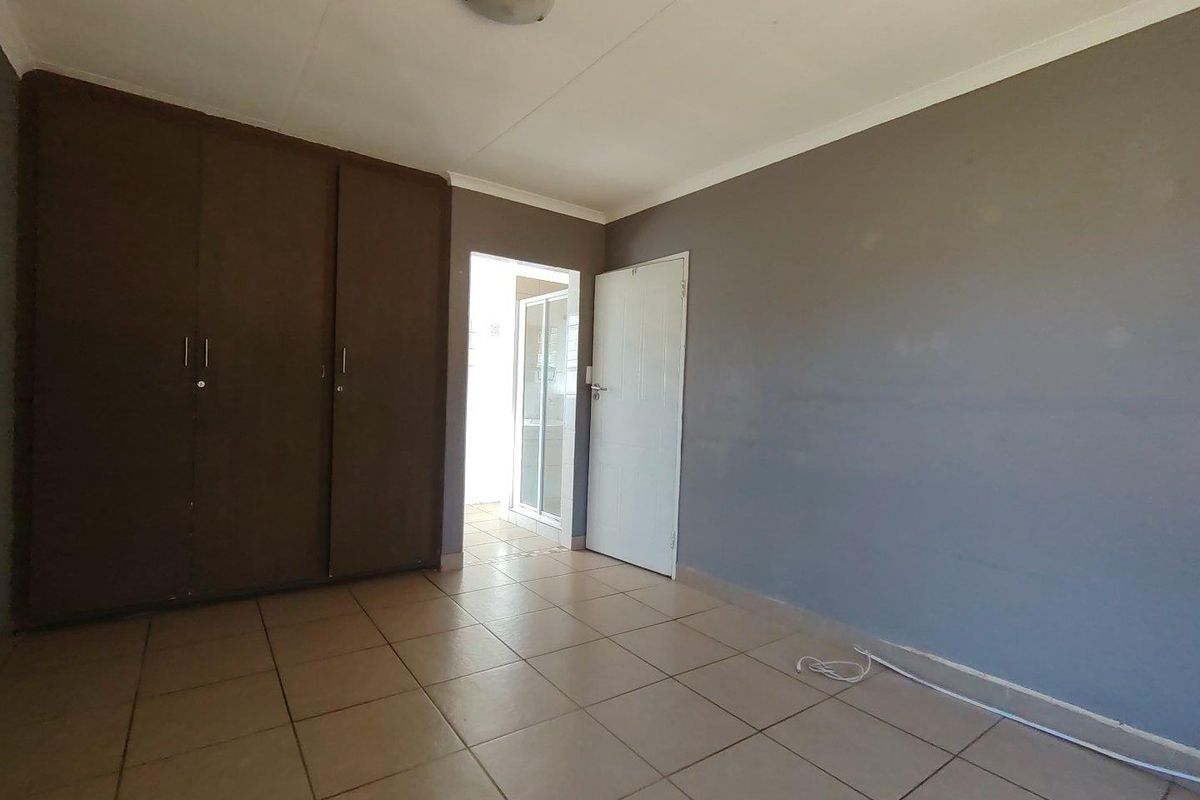 A bedroom featuring built-in cupboards, tiled flooring, and a neutral grey wall finish, providing a functional and blank canvas space.