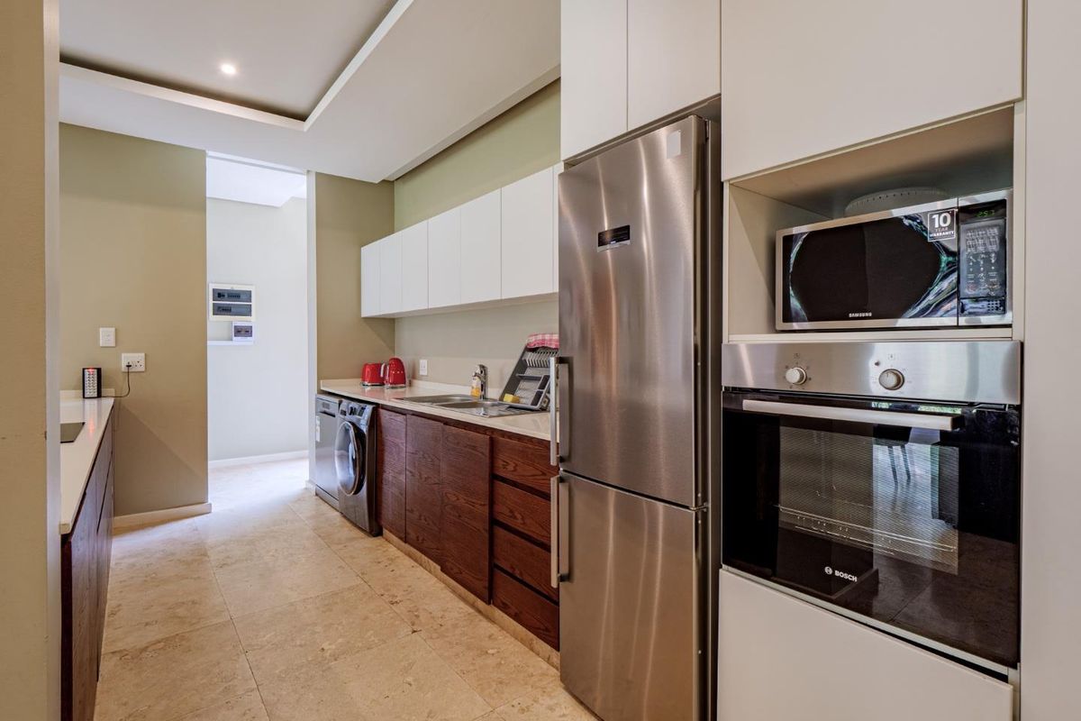 Modern kitchen featuring sleek two-tone cabinetry, stone countertops, integrated stainless steel oven, built-in microwave, and tiled flooring.