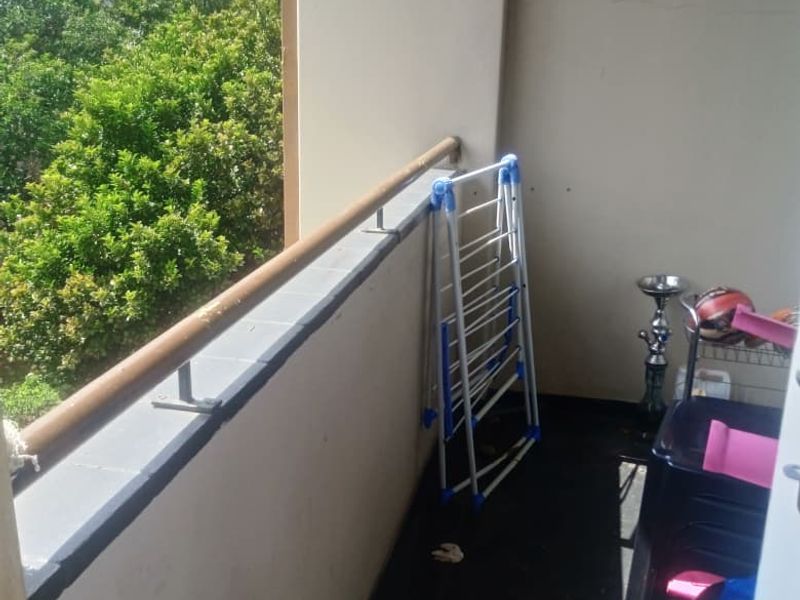 A compact apartment balcony featuring a metal railing and tiled ledge, offering an elevated view of surrounding greenery.