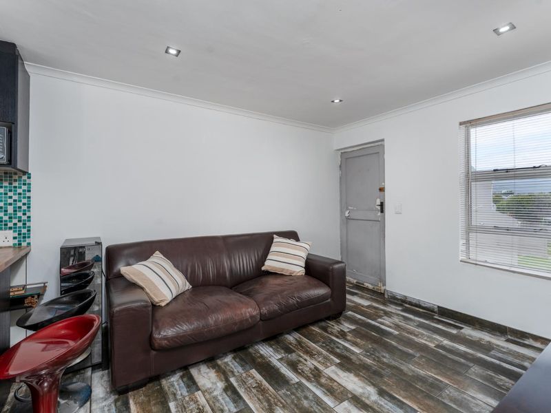 Open plan living area featuring timber-look floor tiles, recessed downlights, and a compact kitchen corner with mosaic tile backsplash and built-in microwave.
