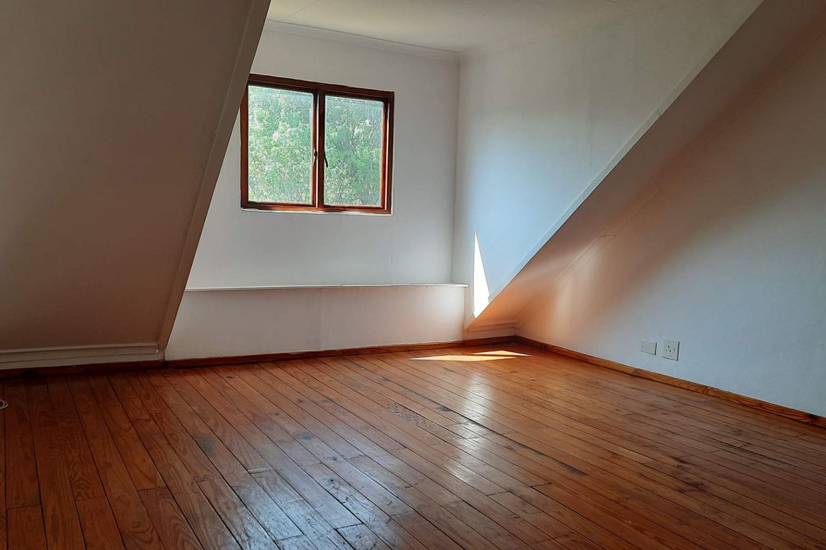 An empty attic-style bedroom featuring polished timber flooring, sloped ceilings, and a timber-framed window providing natural light.