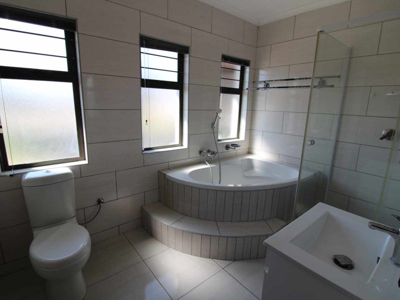 A modern, well-maintained bathroom featuring a corner bathtub, glass-enclosed shower, vanity basin, and neutral floor-to-ceiling tiling.