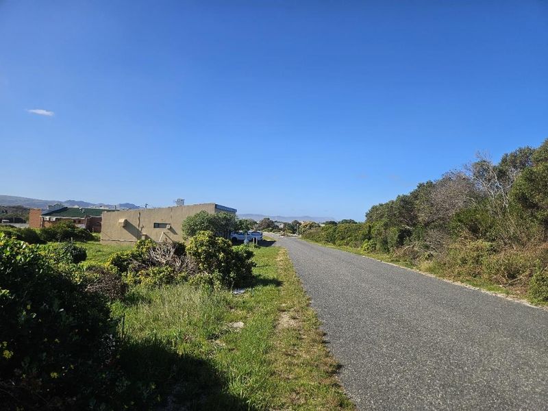 A view of the paved street access leading towards the vacant commercial land, surrounded by natural coastal vegetation.