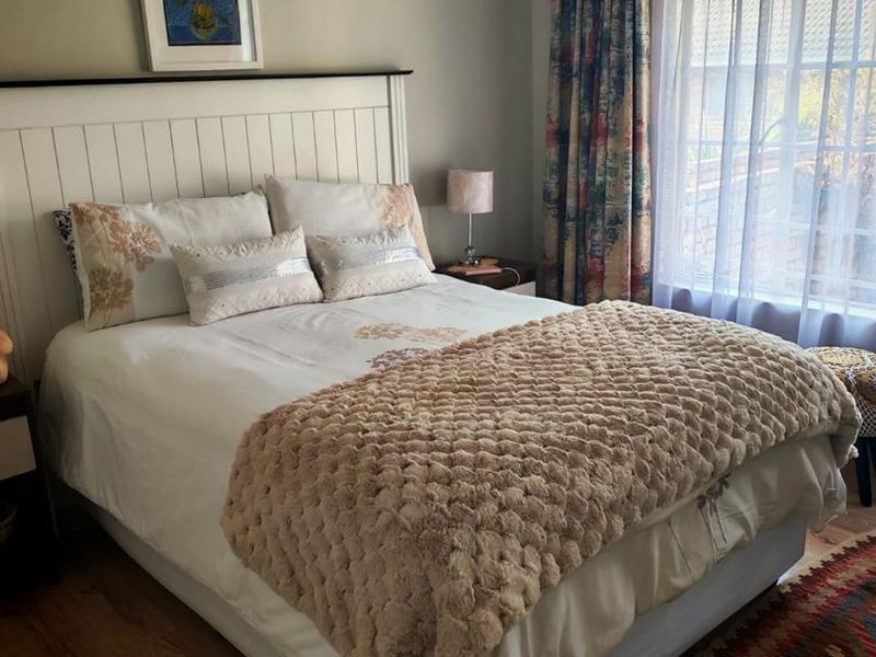 A cozy bedroom featuring laminate flooring, a coved ceiling, and a large window allowing natural light.