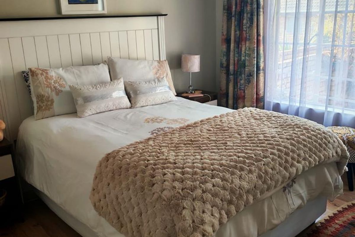 A cozy bedroom featuring laminate flooring, a coved ceiling, and a large window allowing natural light.