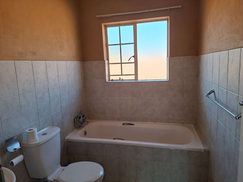 A functional bathroom featuring a built-in bathtub, toilet, and tiled wall finishes, offering a blank canvas for potential cosmetic updates.