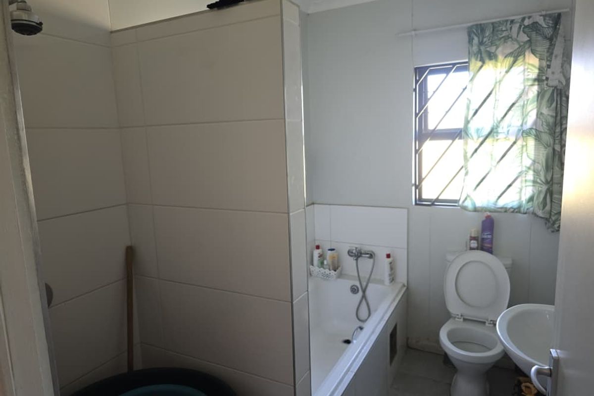 A functional bathroom featuring a tiled shower enclosure, a built-in bathtub, a toilet, and a pedestal basin with security bars on the window.