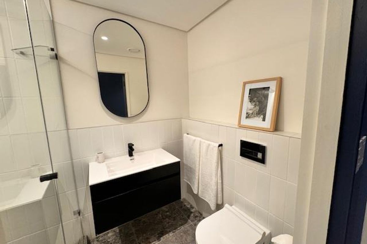 Modern bathroom featuring a wall-mounted vanity, glass-enclosed shower, and a sleek wall-hung toilet with contemporary black fixtures and neutral tiling.