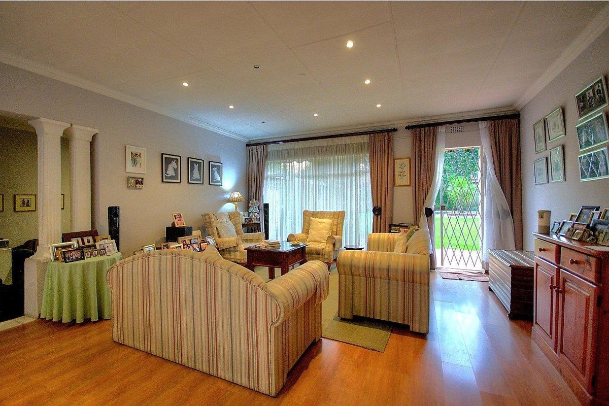 A comfortable living room featuring laminate flooring, recessed ceiling lighting, and direct access to the garden through a glass-paneled security door.
