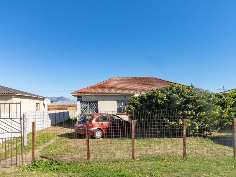 Front view of a single-story residential house featuring a tiled roof, perimeter fencing, and a gated entrance.