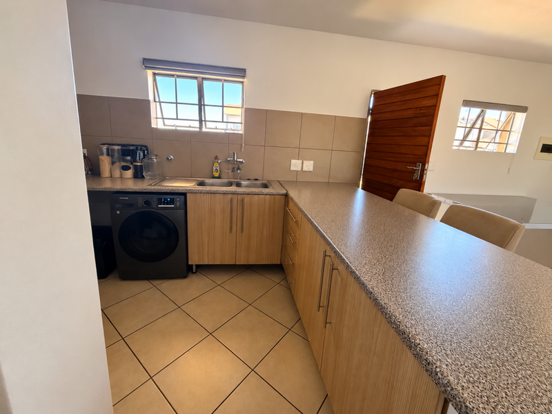 A functional kitchen featuring light wood-finish cabinetry, granite-look countertops, a double sink, and integrated laundry space with tiled flooring throughout.