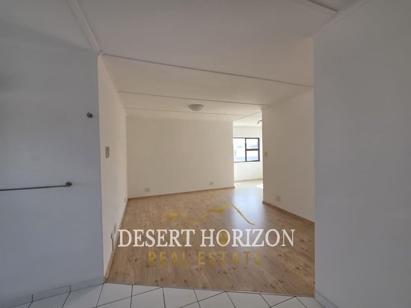 An empty, open-plan living area featuring light-toned laminate flooring and neutral walls, providing a blank canvas for interior design.