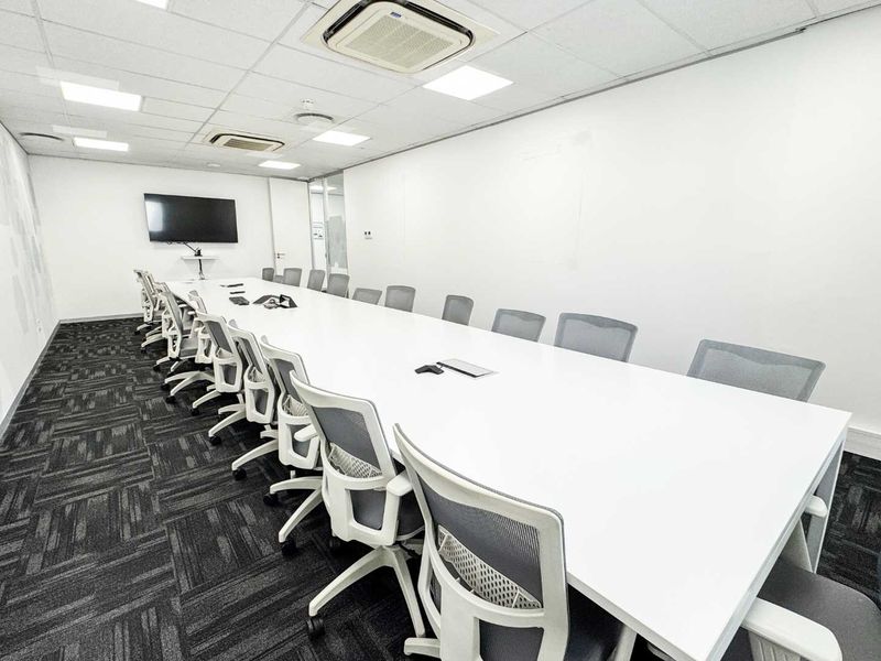 A professional boardroom featuring a long conference table, suspended ceiling with recessed lighting, ducted air conditioning, and modern carpeted flooring.
