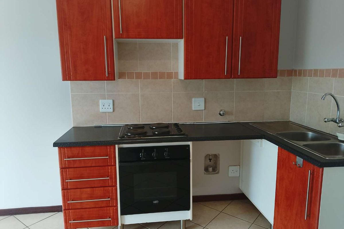 A functional kitchen featuring cherry-wood finish cabinetry, dark laminate countertops, a built-in oven with electric hob, and a stainless steel double sink.