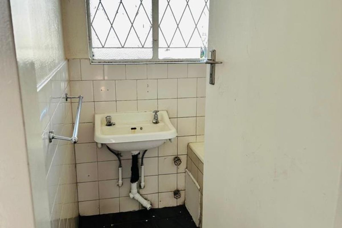 A compact bathroom featuring a wall-mounted basin, tiled splashback, and leaded glass window. The space requires renovation to update dated finishes and plumbing fixtures.