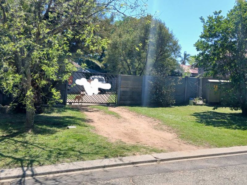 Street view of the property entrance featuring a metal gate, perimeter fencing, and an unpaved driveway leading to the residence.