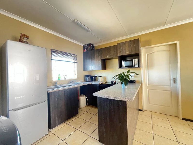 A functional kitchen featuring dark wood-look cabinetry, granite-style countertops, a built-in microwave, and tiled flooring with a breakfast counter.