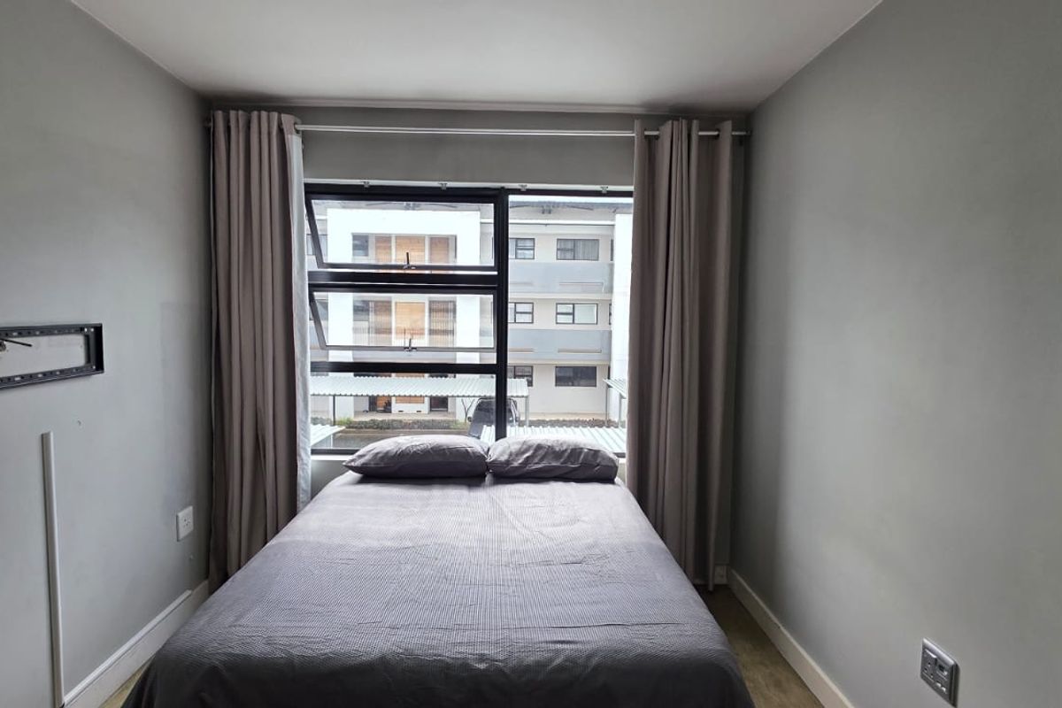 A compact bedroom featuring neutral grey walls, aluminium window frames, and fitted skirting boards, providing a clean and functional living space.