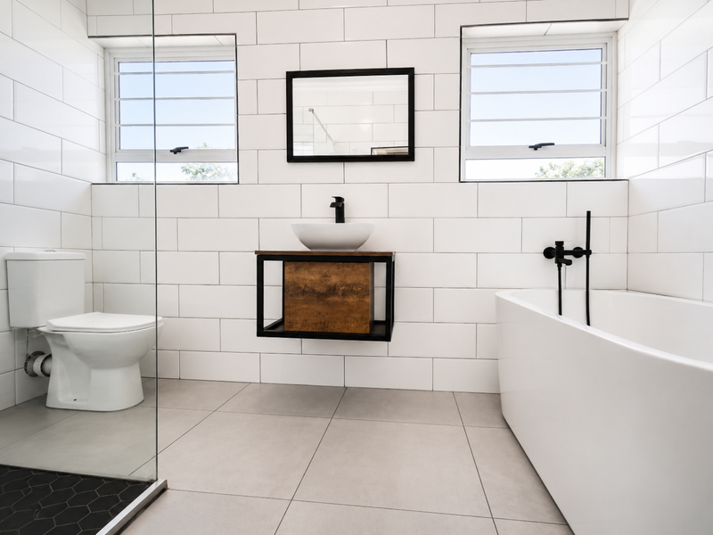 Modern bathroom featuring white subway wall tiles, a floating vanity with vessel sink, black tapware, a freestanding bathtub, and a glass-enclosed shower area.