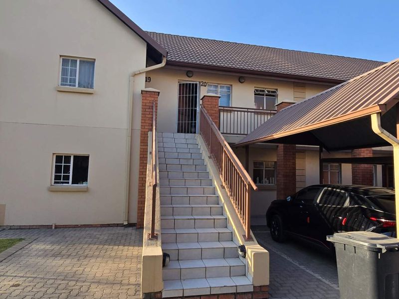 Exterior view of an apartment unit featuring a private tiled staircase entrance, brick accents, and an adjacent covered carport parking area.