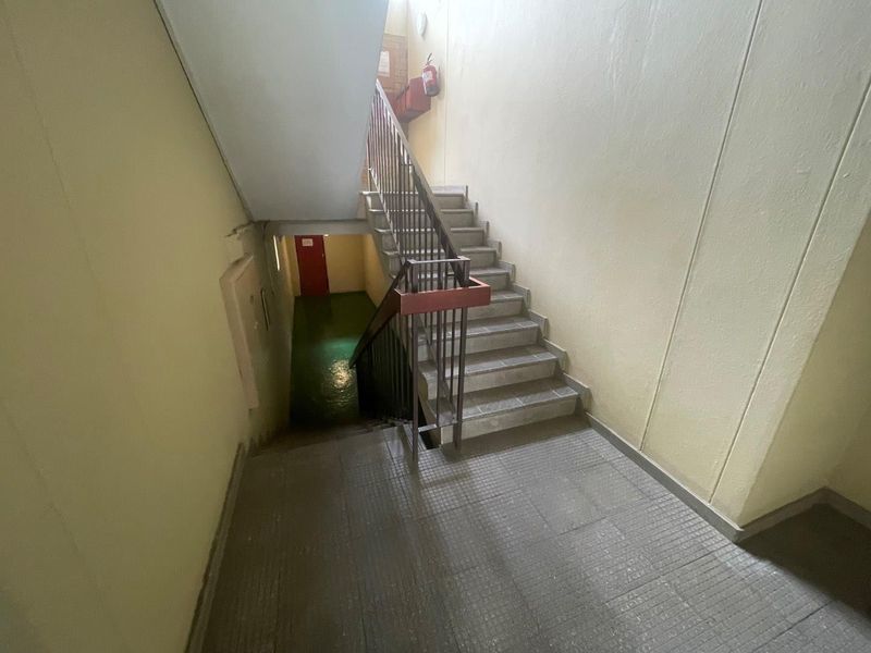 A functional apartment building stairwell featuring a metal handrail and basic tiled flooring, providing access between levels.