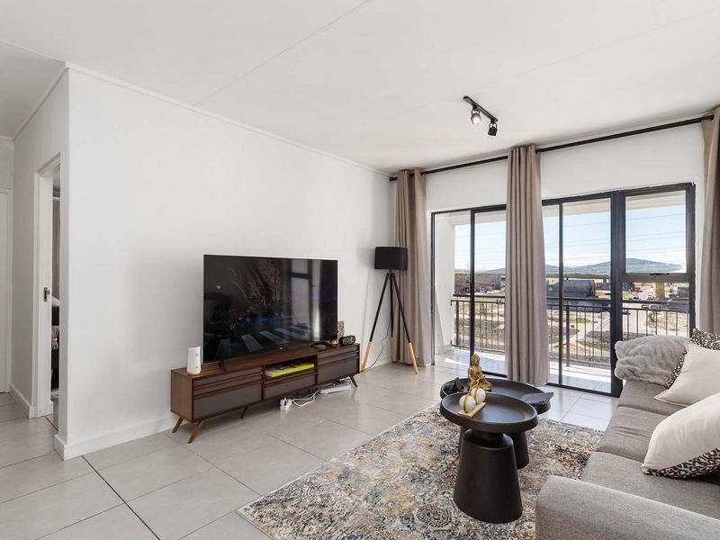 Bright living room featuring neutral tiled flooring, modern track lighting, and large sliding glass doors providing access to a private balcony.