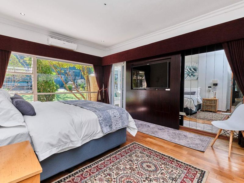 Spacious bedroom featuring hardwood flooring, mirrored built-in wardrobes, split-system air conditioning, and large windows overlooking the garden.
