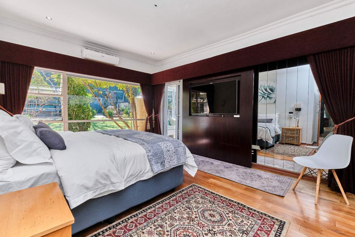 Spacious bedroom featuring hardwood flooring, mirrored built-in wardrobes, split-system air conditioning, and large windows overlooking the garden.