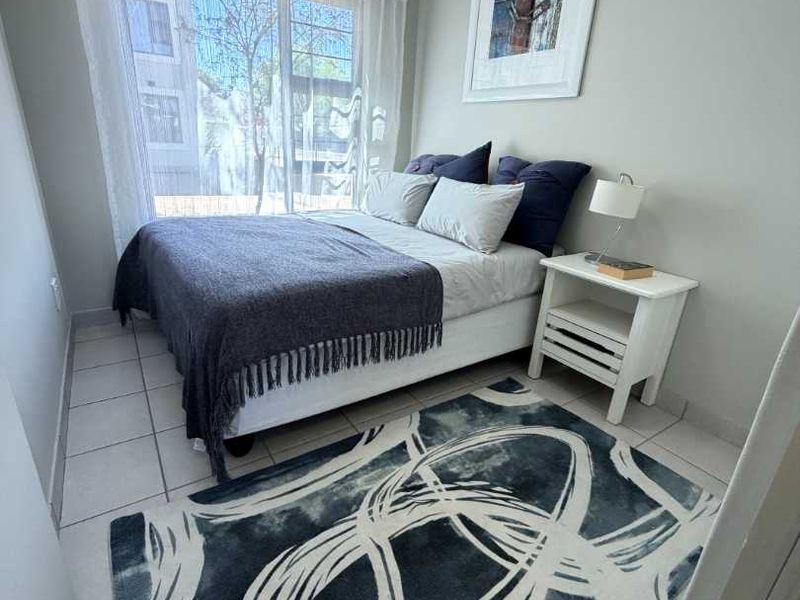 A well-lit bedroom featuring neutral wall tones, tiled flooring, and a large window providing natural light.