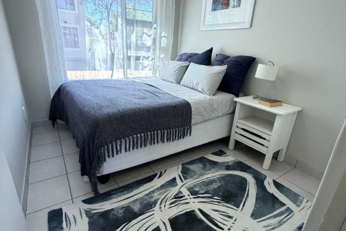 A well-lit bedroom featuring neutral wall tones, tiled flooring, and a large window providing natural light.