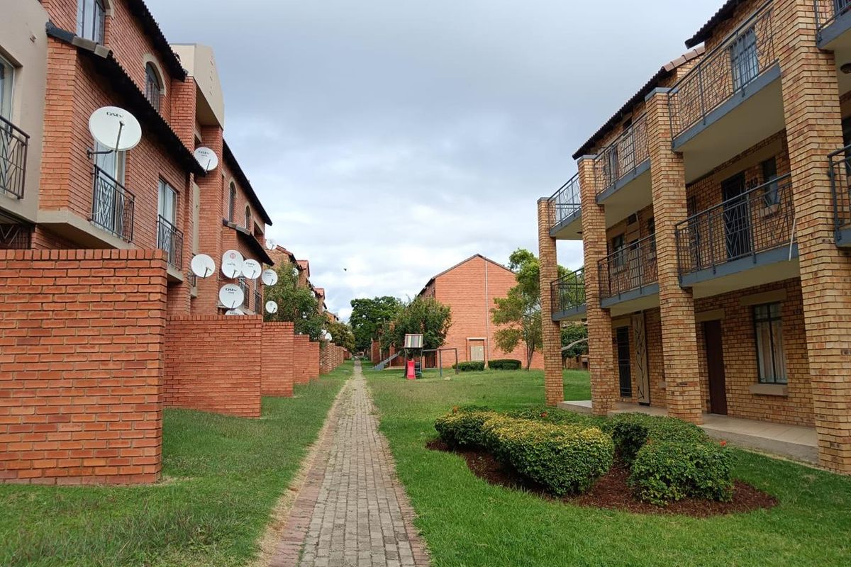 Exterior view of a brick apartment complex featuring paved walkways, landscaped garden areas, and multiple satellite dishes mounted on the building facades.