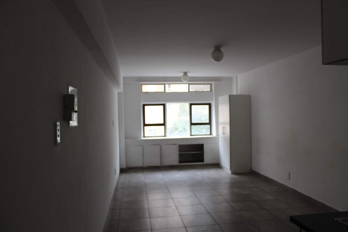 An empty, open-plan living area featuring tiled flooring, built-in cabinetry, and large windows providing natural light.