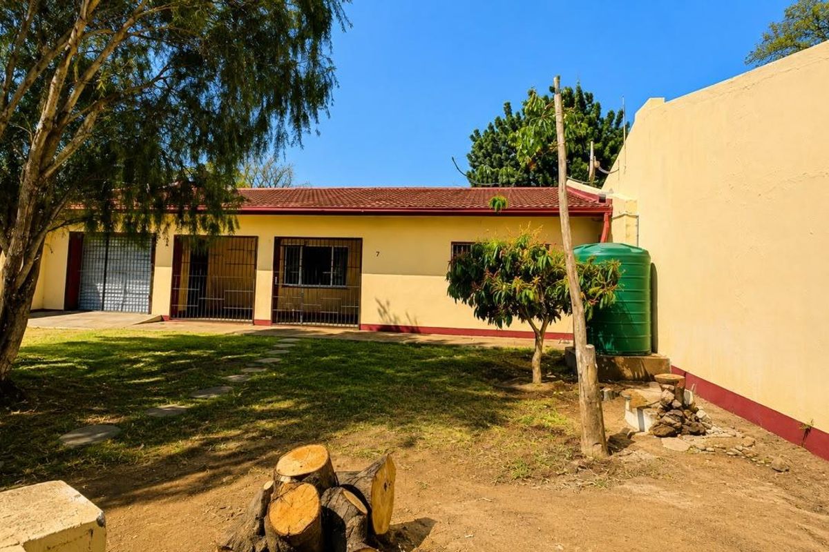 Rear exterior view of the townhouse featuring a garden area, security gates, and a water storage tank against a boundary wall.