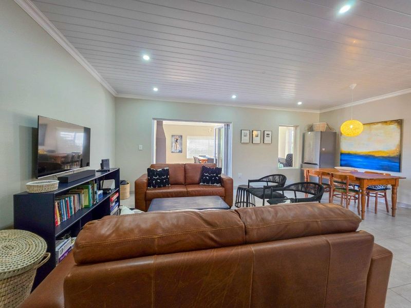 Spacious open-plan living and dining area featuring tiled floors, recessed downlighting, and a distinctive tongue and groove ceiling with access to an outdoor space.