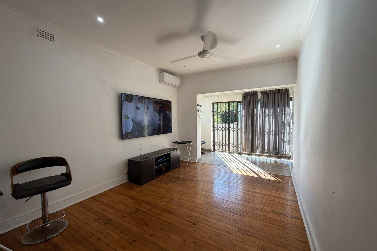 A living room featuring hardwood flooring, a ceiling fan, recessed lighting, and a split-system air conditioner, with access to an outdoor area via a security gate.