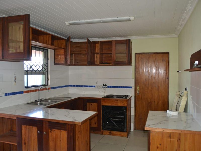 Functional kitchen featuring wooden cabinetry, marble-look countertops, a built-in oven and hob, and a double sink with tiled splashback.