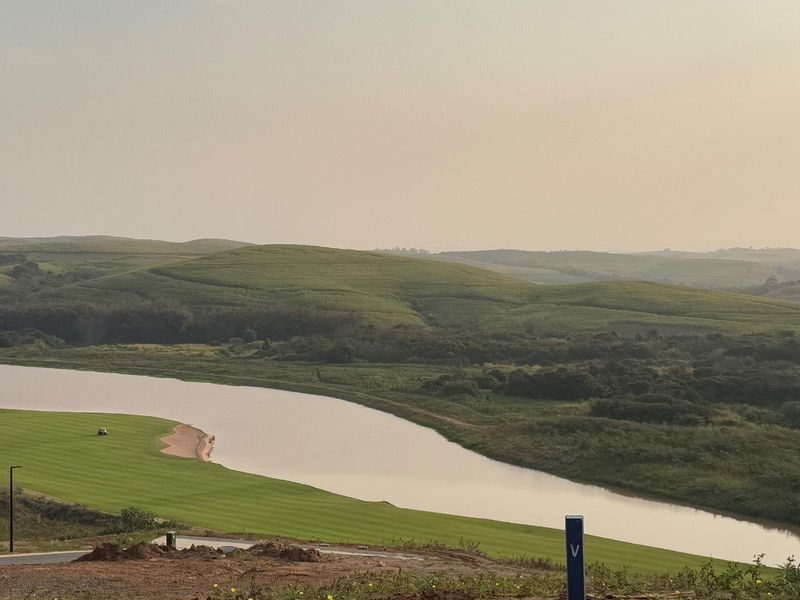 A scenic elevated view overlooking a golf course, river, and rolling green hills, showcasing the natural landscape of the vacant residential land.