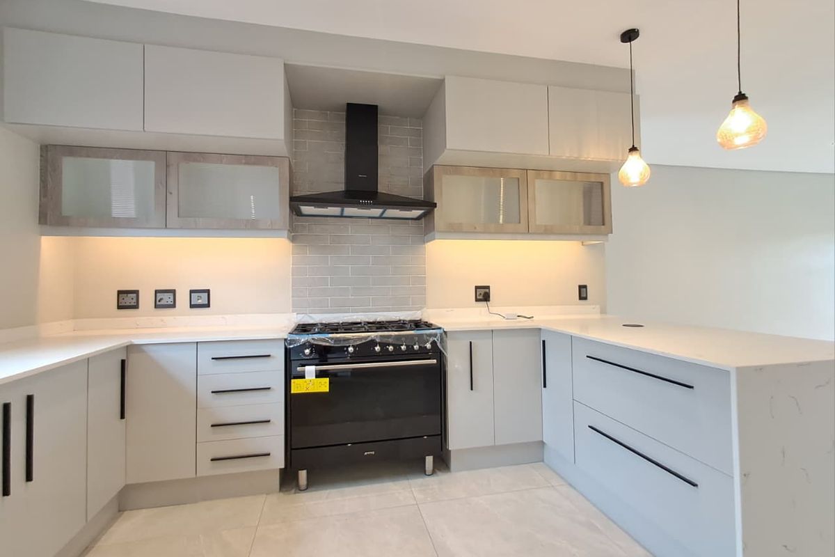 Modern kitchen featuring light grey cabinetry, quartz countertops, subway tile backsplash, and a black freestanding gas stove with matching extractor fan.