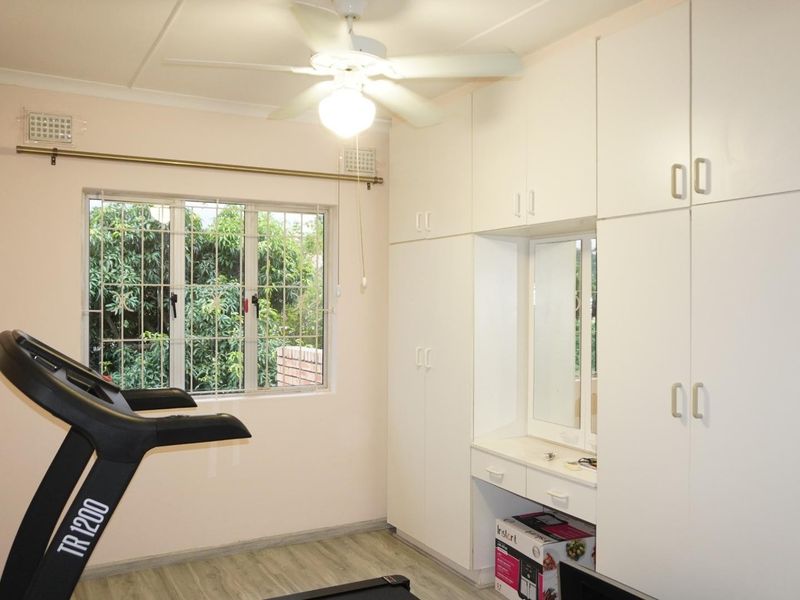 Bedroom featuring extensive built-in cabinetry with a central vanity, ceiling fan, air conditioning, and security bars on the window.