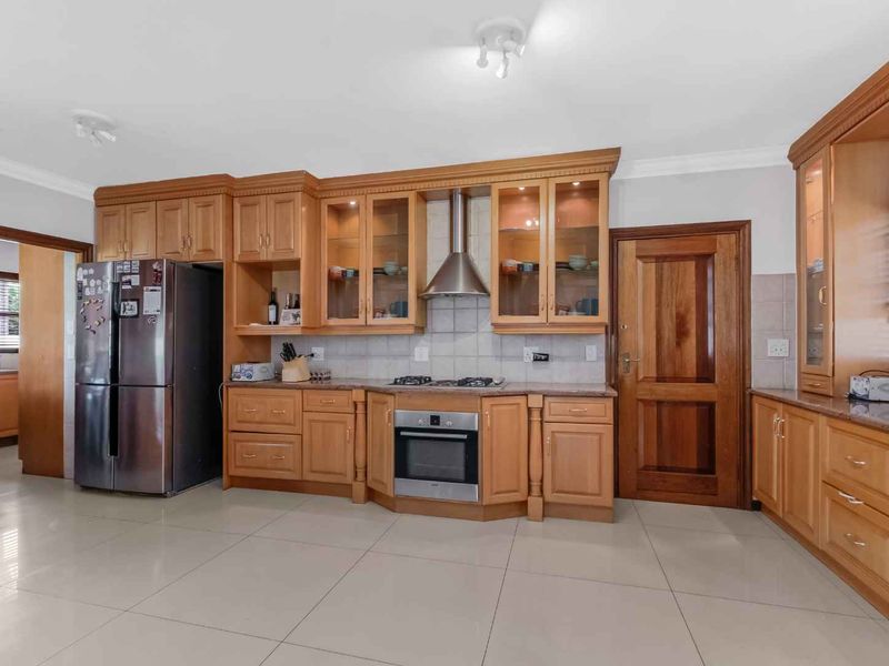 Spacious kitchen featuring warm-toned wooden cabinetry, granite countertops, integrated stainless steel appliances, and neutral tiled flooring throughout.
