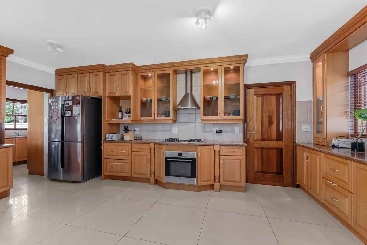 Spacious kitchen featuring warm-toned wooden cabinetry, granite countertops, integrated stainless steel appliances, and neutral tiled flooring throughout.