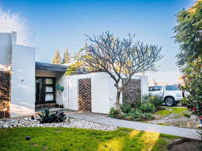 Front elevation of a modern house featuring a combination of brick and plastered walls, a concrete walkway, and a landscaped front garden.