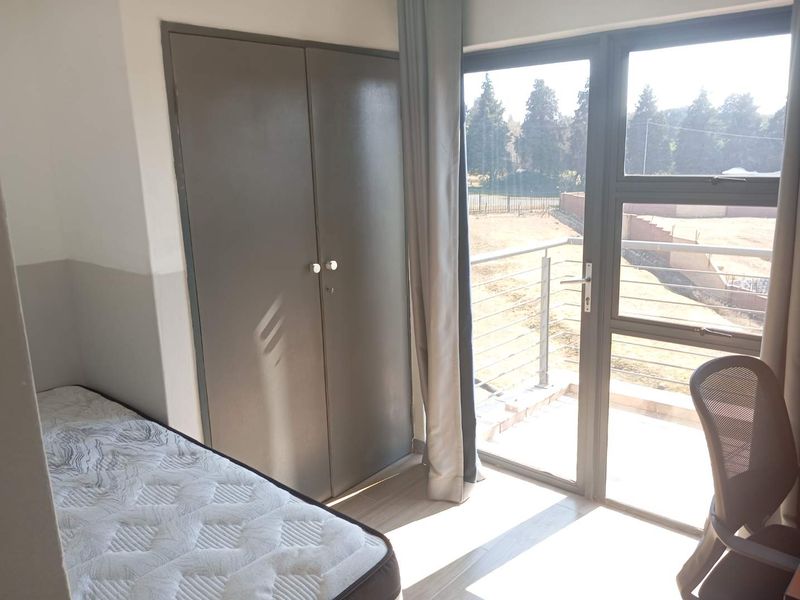 A bright bedroom featuring laminate flooring, a built-in wardrobe, and direct access to a private balcony through an aluminium sliding door.