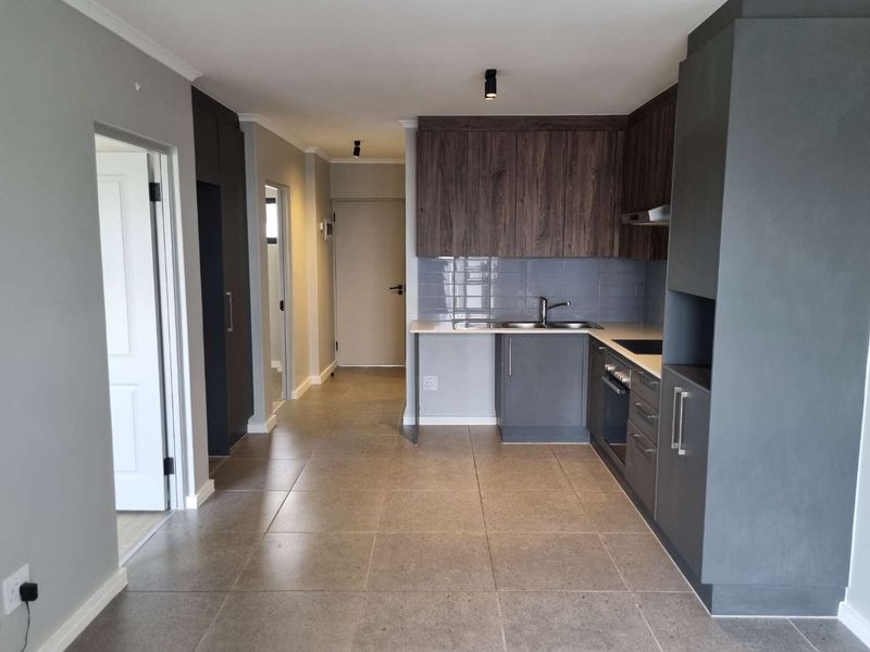 Modern kitchen featuring sleek dark cabinetry, subway tile backsplash, integrated appliances, and neutral tiled flooring in an open-plan layout.