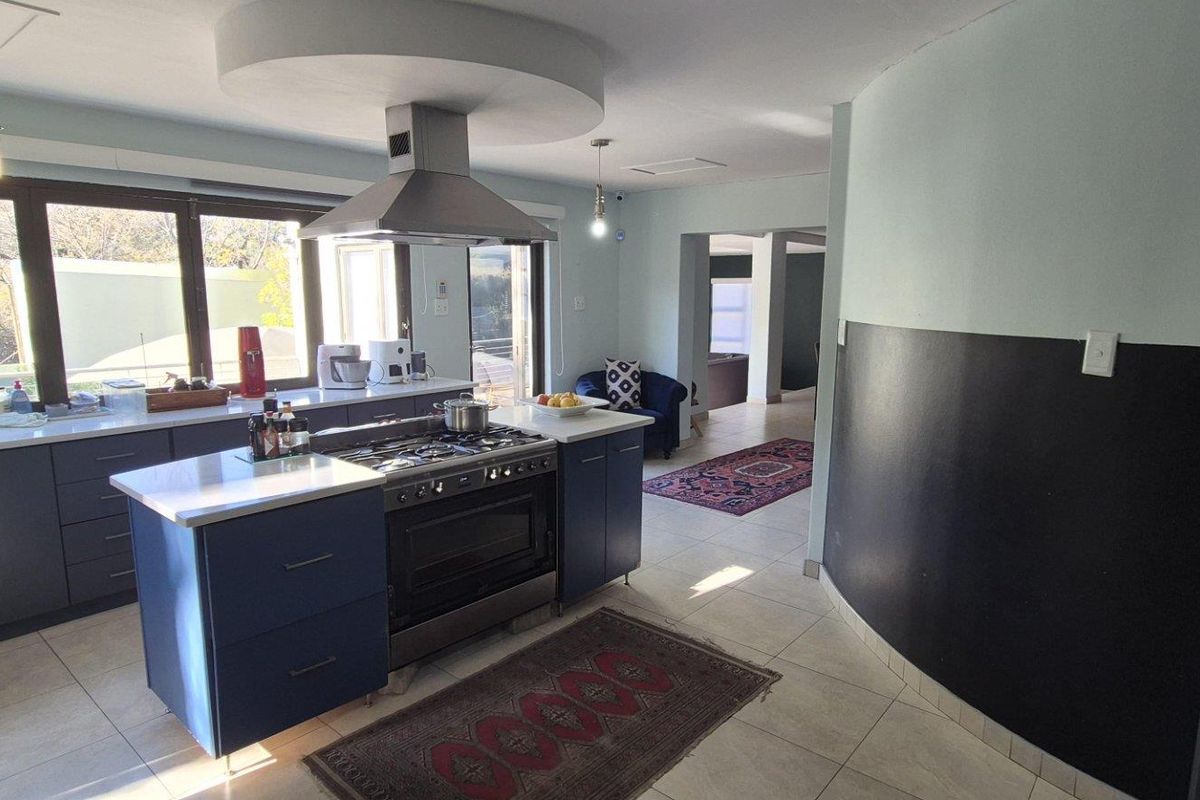 Modern kitchen featuring a central island with a gas stove, extractor fan, ample cabinetry, and tiled flooring, flowing into an adjacent living area.