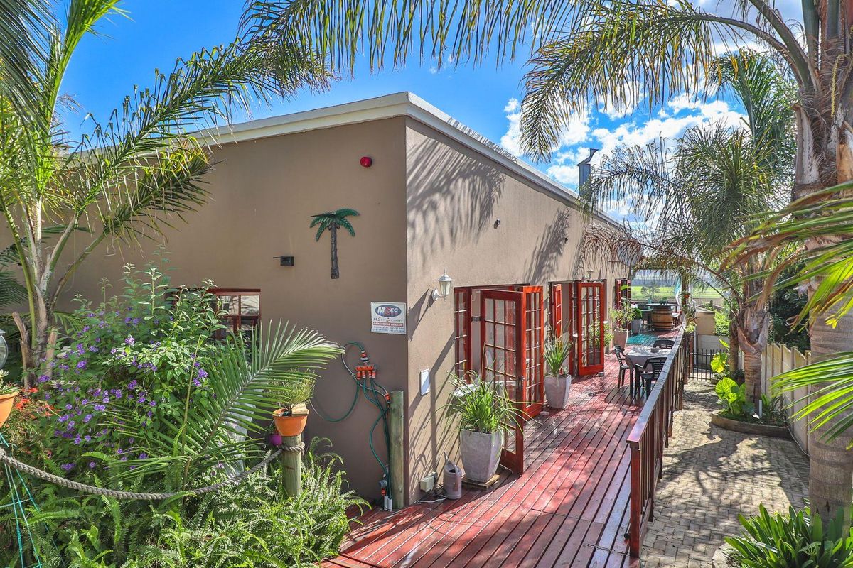 A rear exterior view featuring a raised timber deck, multiple sets of wooden French doors, and established garden landscaping.