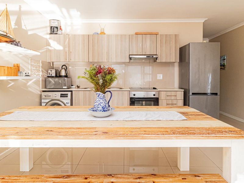 Open-plan kitchen area featuring light wood-finish cabinetry, integrated appliances, and polished tiled flooring, seamlessly connecting to the dining space.